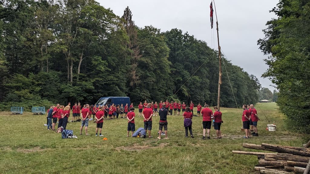A large circle of Scouts in neckers gathered round a flagpole in a forest clearing